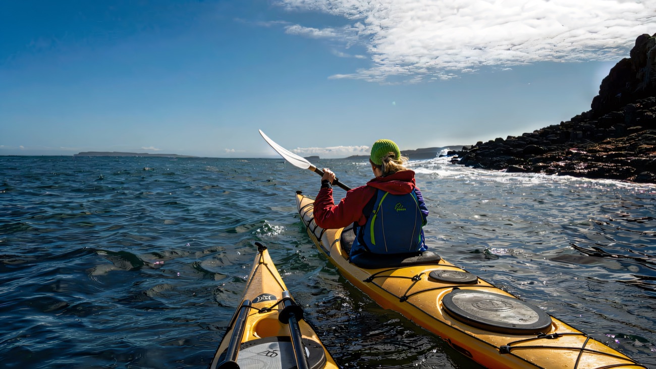 Paddling out along the basalt coastline under a big blue sky