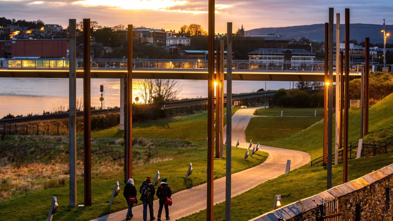 The path drops to the riverside with the Peace Bridge and Derry beyond