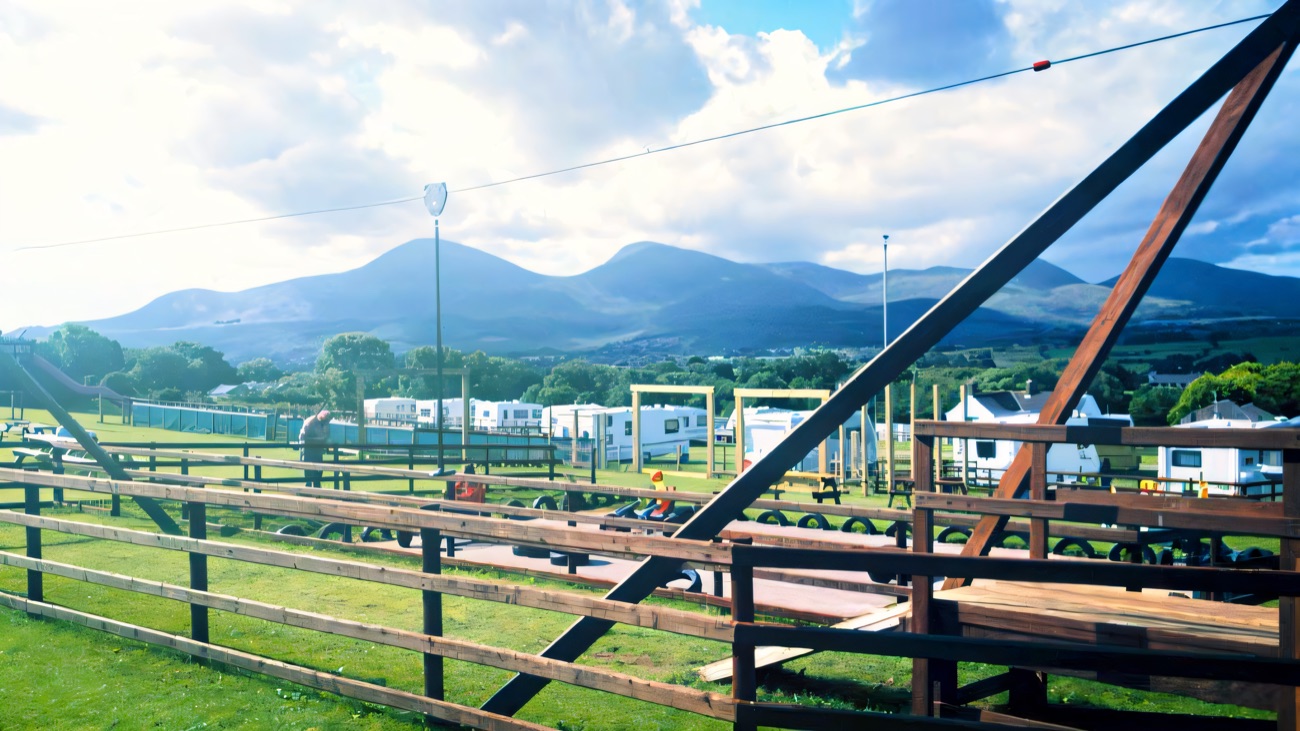 Picnic benches, a zip-line frame and play area in front of the Mourne Mountains at the farm