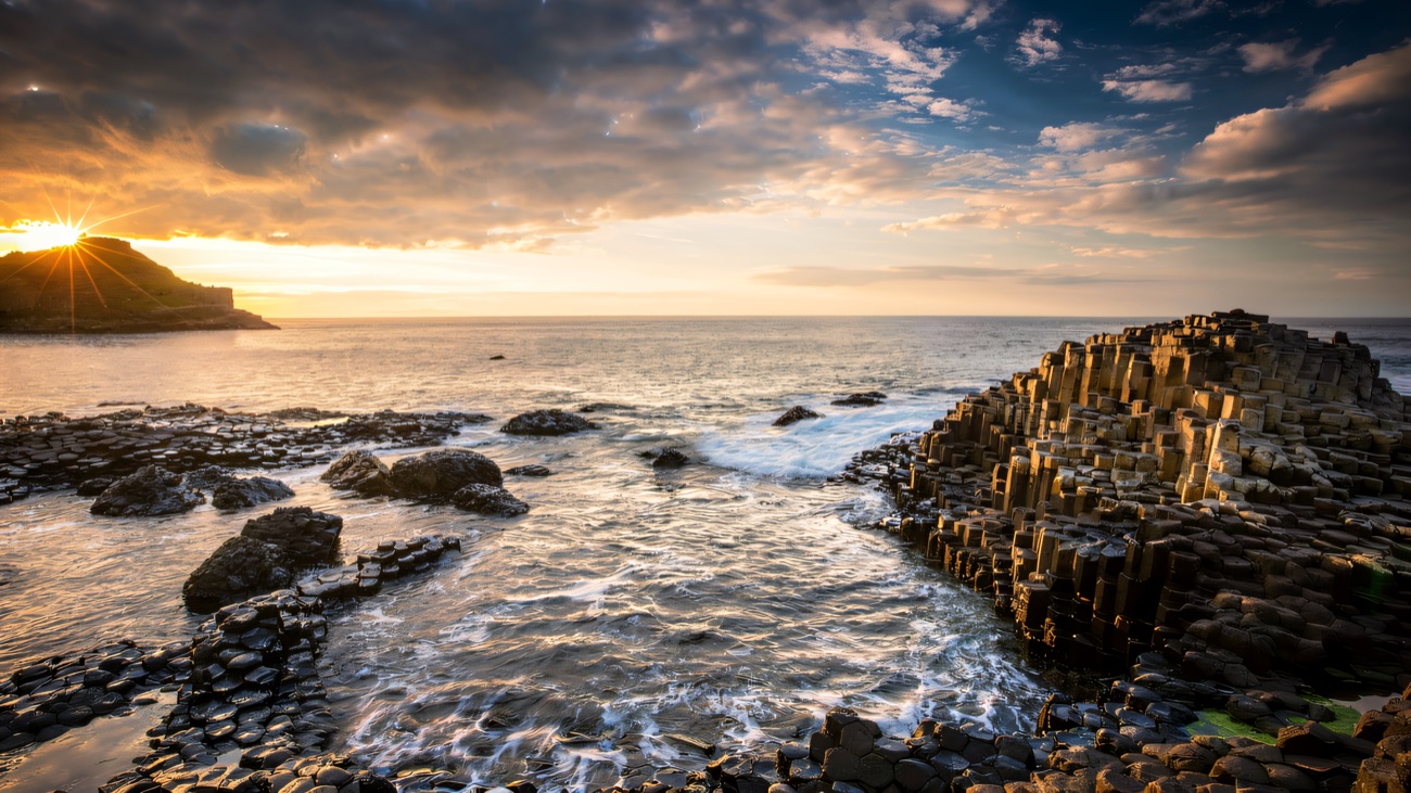 The sun bursts low over the water in a golden evening at the Causeway.