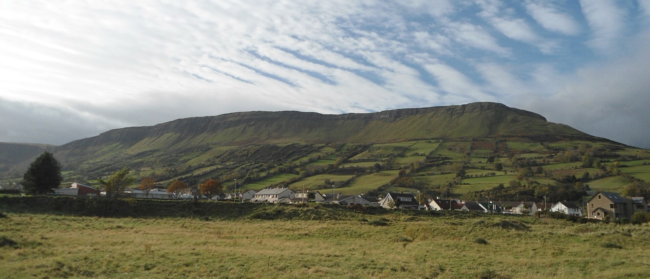 A wide view of the green glen with the flat-topped Lurigethan mountain rising behind.