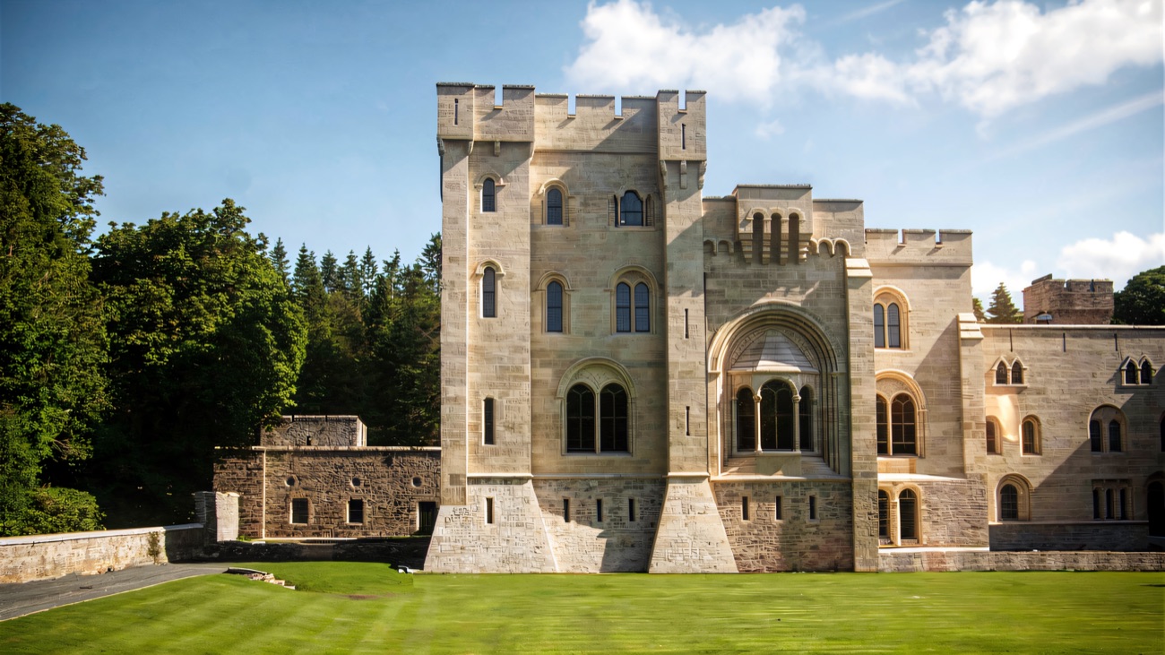A battlemented stone tower and arched window of Gosford Castle under a blue sky above a striped green lawn