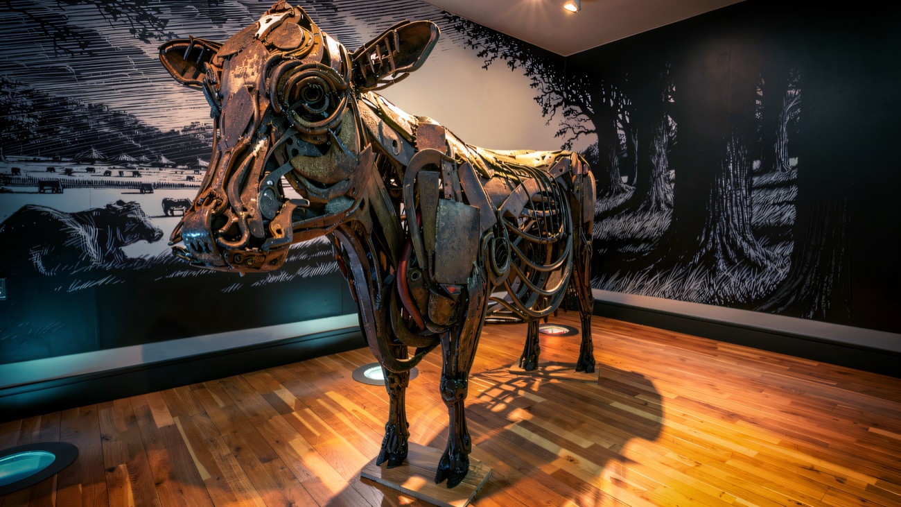 A striking beaten-metal cow sculpture set against a black-and-white pastoral mural.