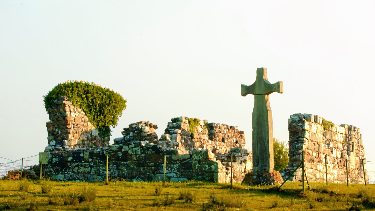 A wider view of the church walls and cross set in the island grass.