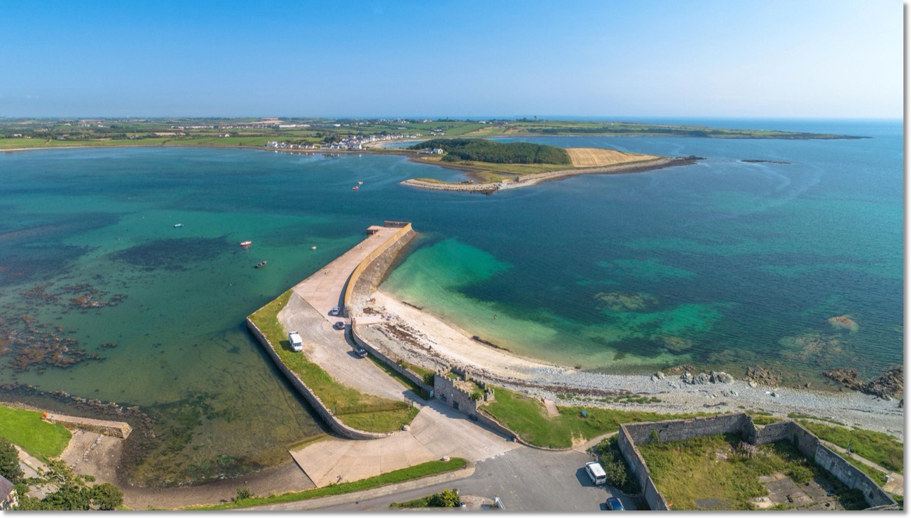 Aerial view of the long Killough harbour pier curving into the clear turquoise water of Coney Island Bay on a bright day