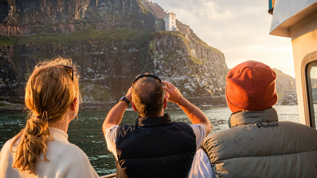Passengers watch a clifftop lighthouse slide past as the boat rounds the headland