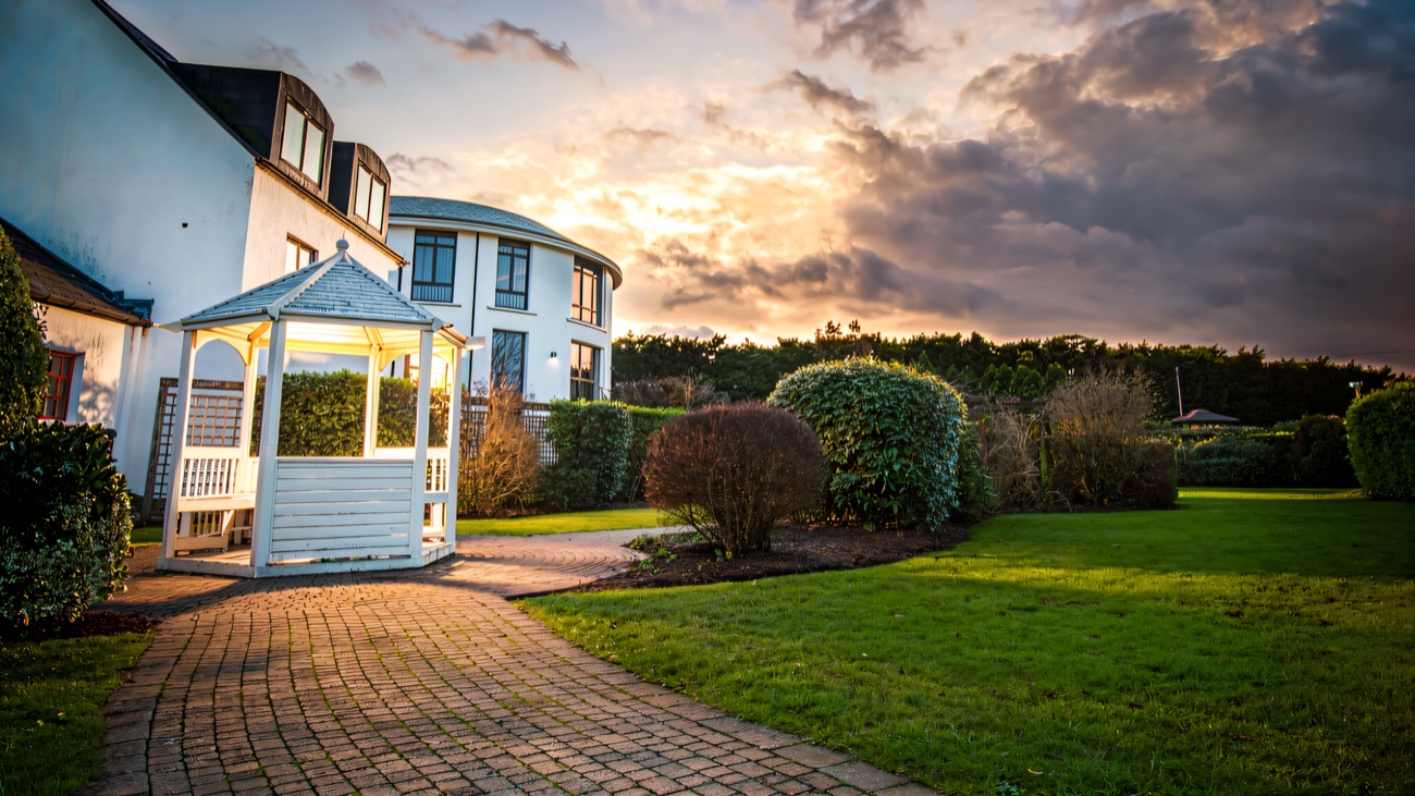 A white timber gazebo and neat lawns in the hotel gardens under an evening sky.