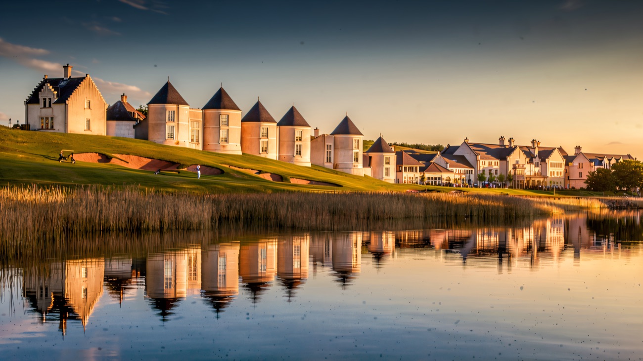 The resort's turrets glow gold at sunset, mirrored in the still lough.