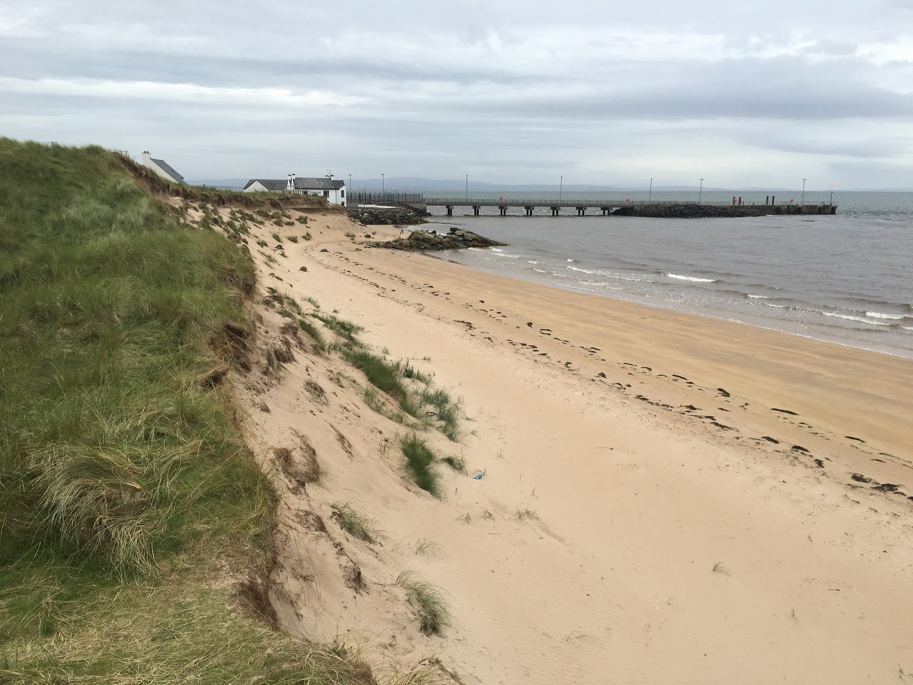 The wide sandy beach and eroding dunes at Magilligan Point with the ferry pier and Lough Foyle beyond under a cloudy sky