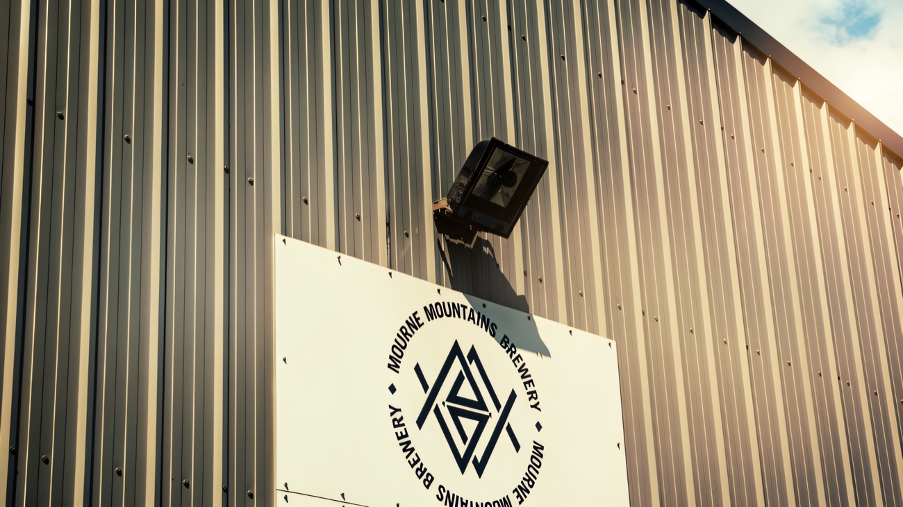 The brewery's sign mounted on the grey metal-clad wall of the building, under a bright blue sky.