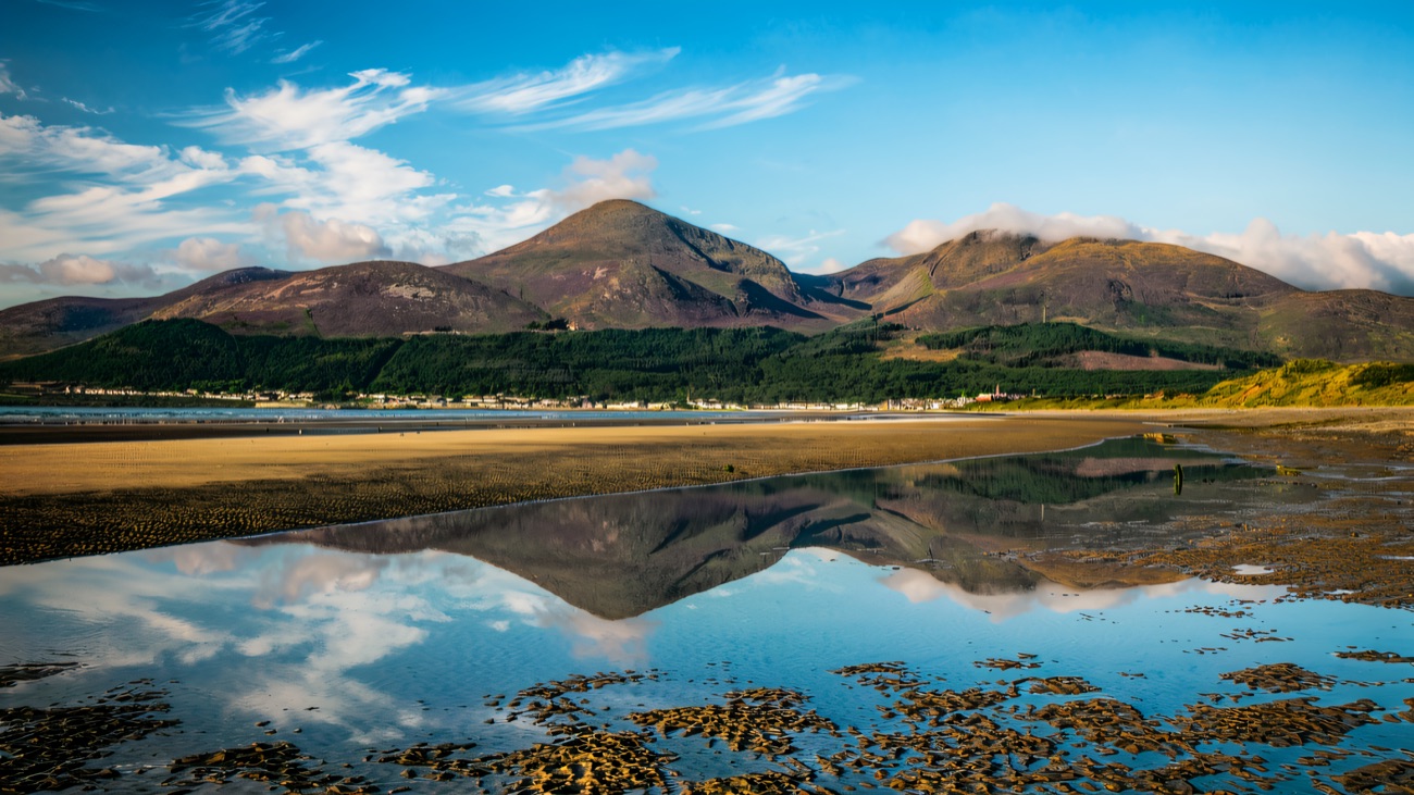 The wide flat beach at Murlough with the Mourne Mountains reflected in a tidal pool under blue sky