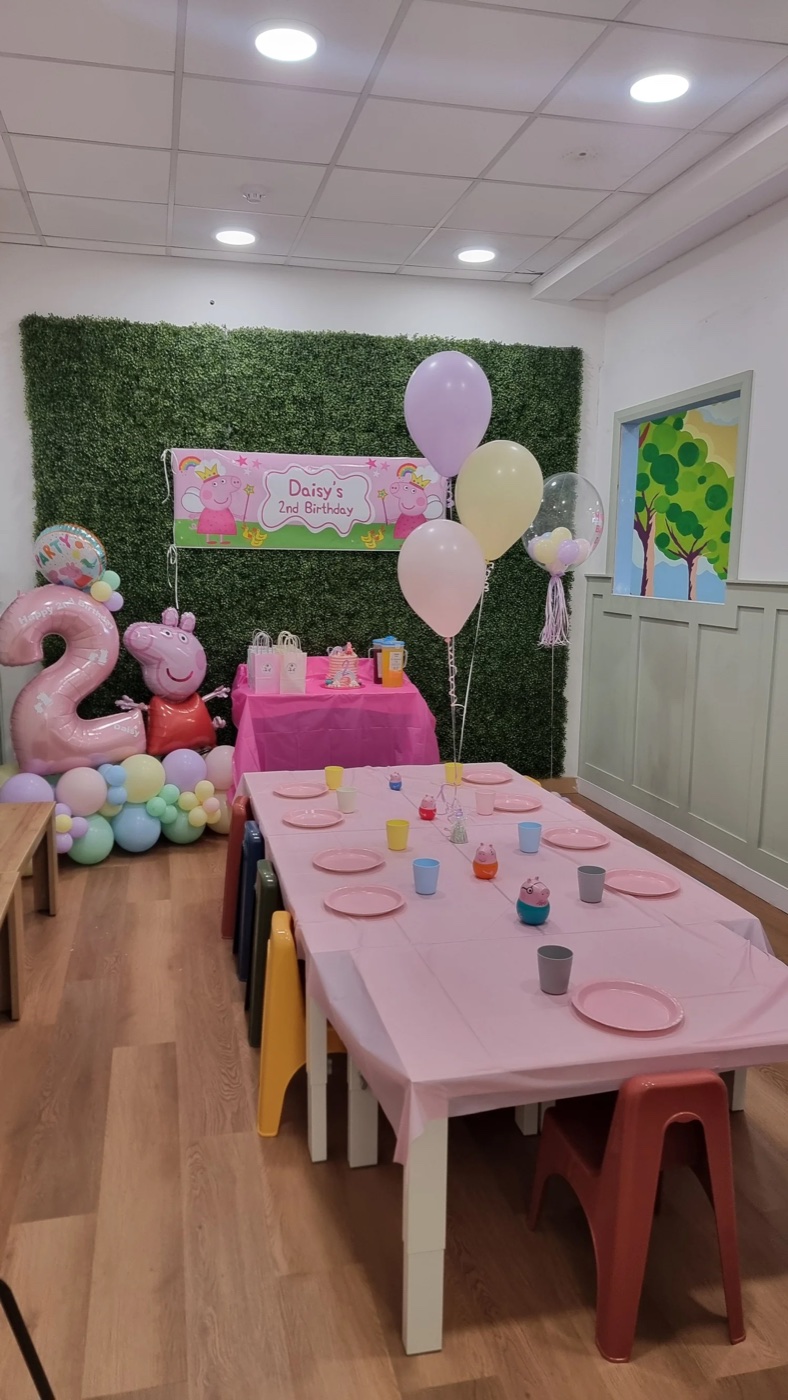A party area at Nature and Nurture in Lisburn, with a greenery wall, a pink party table set with cups and plates, and pastel balloons