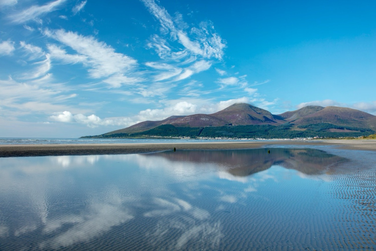 The Mourne Mountains mirrored in a still tidal pool on Newcastle beach under a bright blue sky