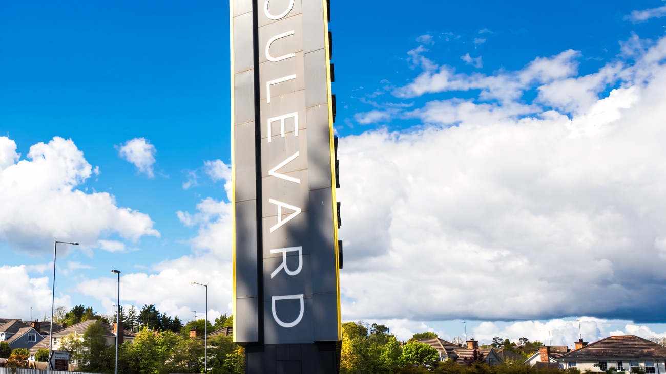 The tall grey Boulevard totem sign standing at the entrance to the outlet village off the A1 at Banbridge, under a bright blue sky