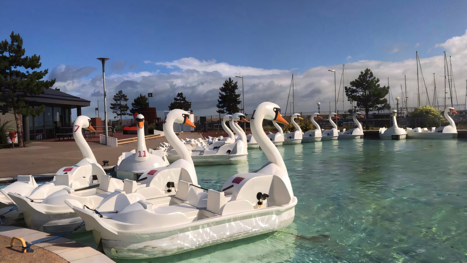 The famous giant white swan pedal boats moored on the turquoise boating lake at Pickie Funpark, marina behind