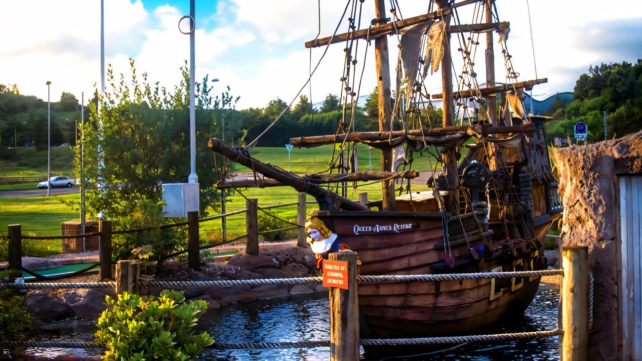 The full-rigged pirate ship Queen Anne's Revenge flying a Jolly Roger, moored in the course's water hazard beside a putting green