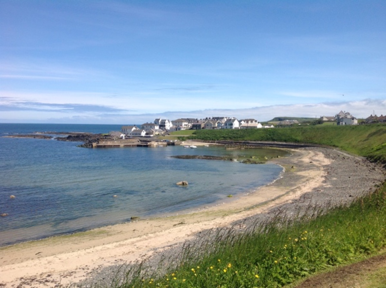The sheltered bay and beach at Portballintrae village with houses lining the shore on a sunny day