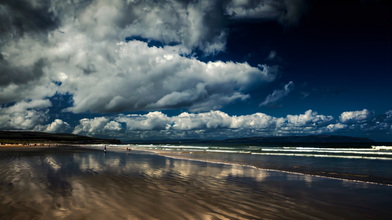 Wide reflective sands under a towering summer sky