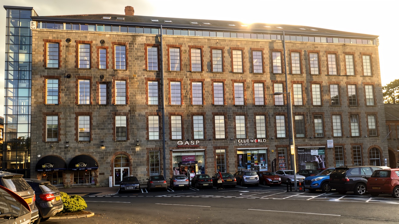 The tall stone face of Drumalane Mill, the old mill building folded into The Quays complex, with shop units at street level