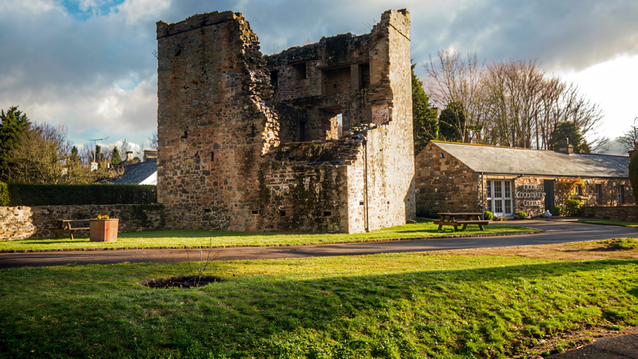 The ruined stone tower house standing beside the site building on a bright day