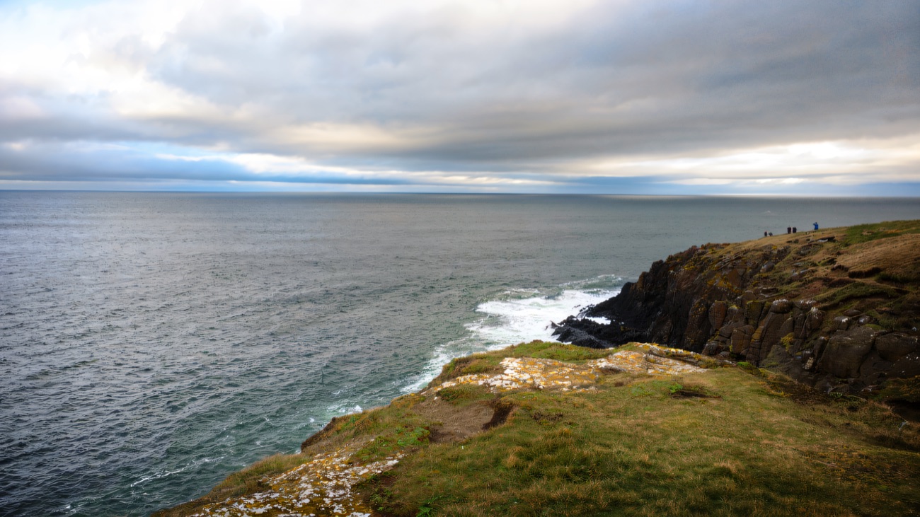 A moody clifftop view out over the sea from the grassy head