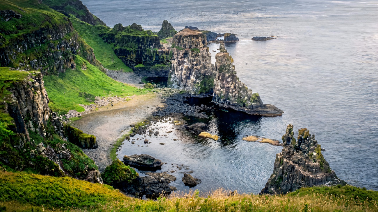 Jagged sea stacks and a pebble cove below the grassy cliff tops of the island's west end.