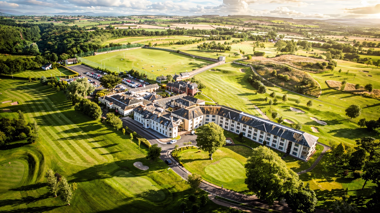 The resort seen from the air, wrapped in green golf-course parkland with the hills beyond.