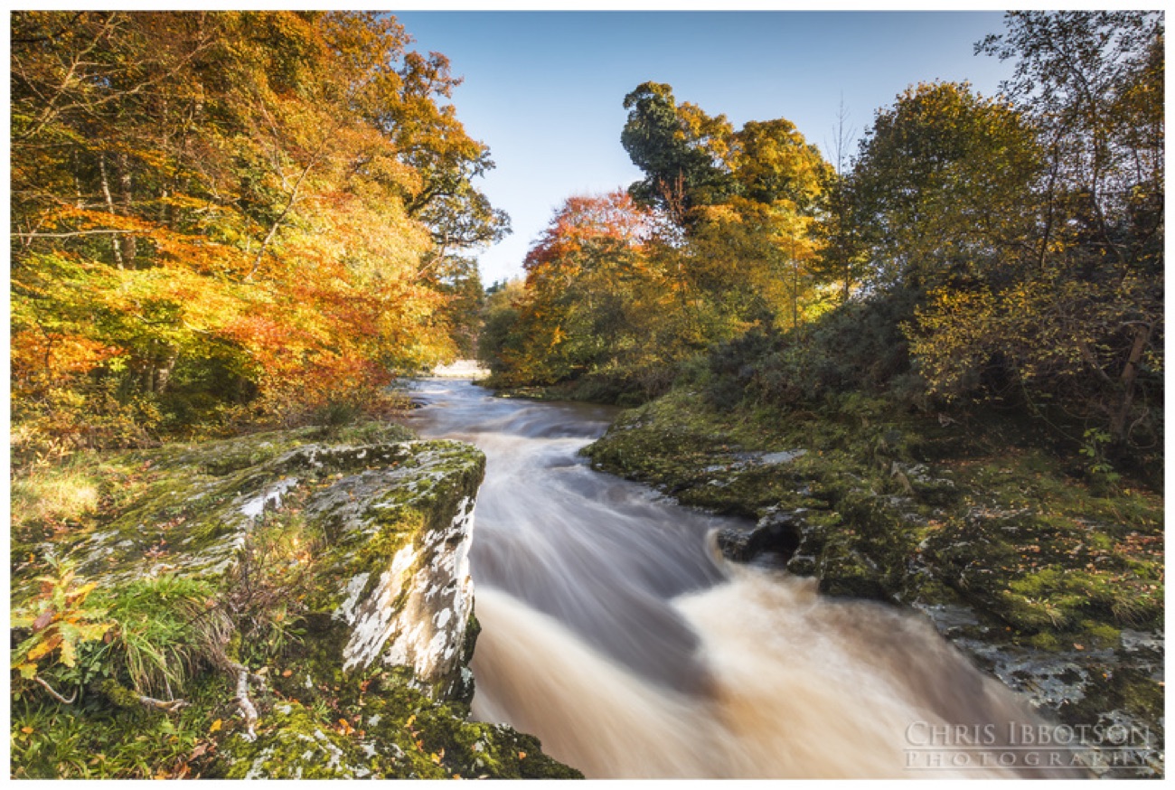 Autumn colour frames the river as it rushes white over a rocky drop in the gorge.