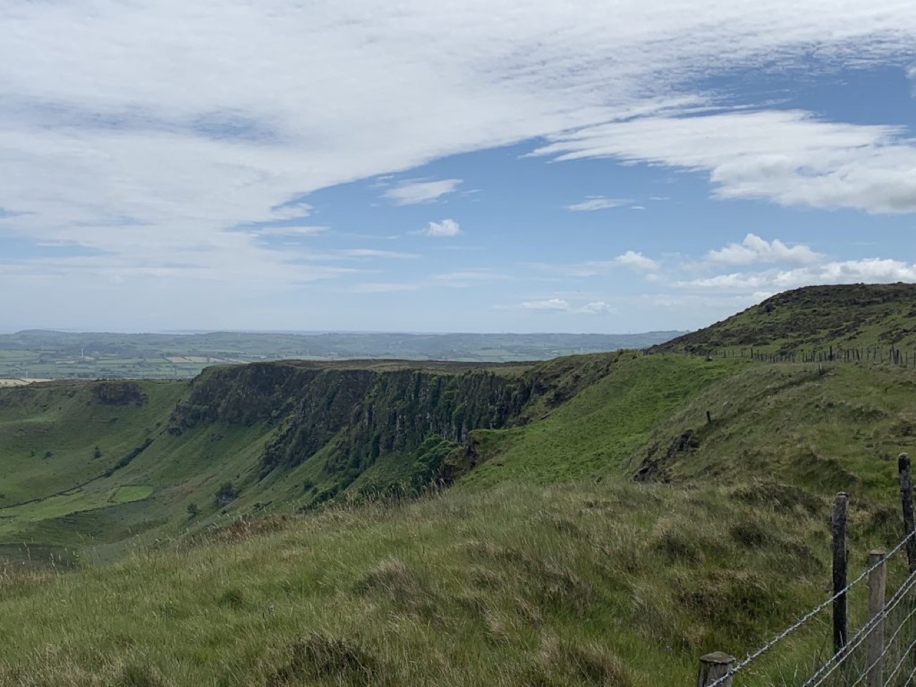 The green horseshoe of Sallagh Braes under a blue sky, with heather and a hilltop fence in the foreground