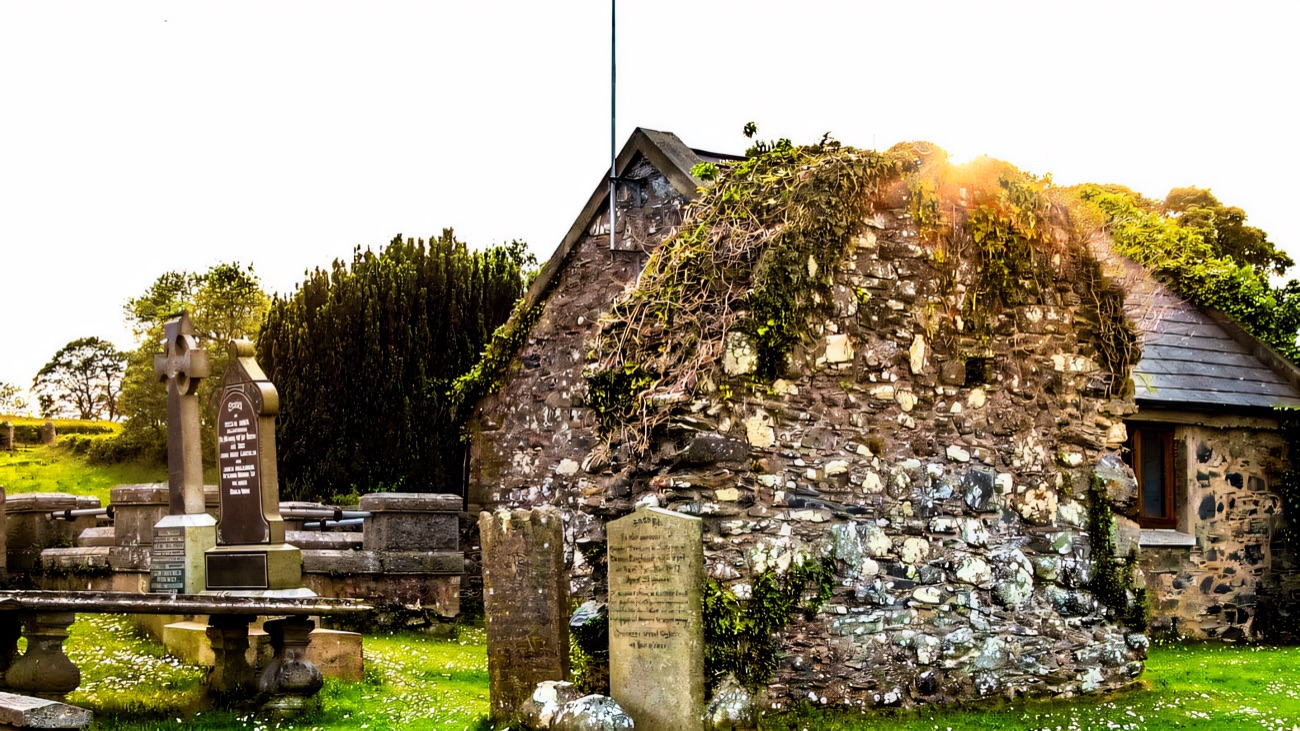 The older ruined stone building and headstones in the graveyard beside the church.