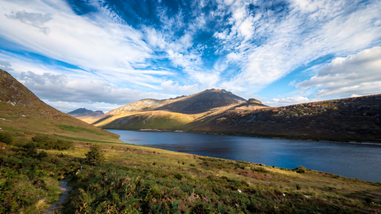 A stony path beside the reservoir with the Mourne Mountains rising under a big blue sky