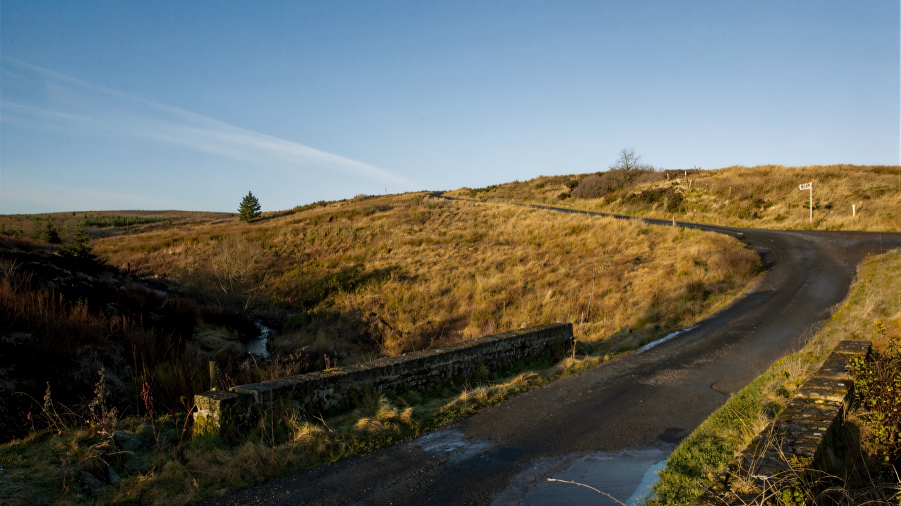 The narrow lane winding over the bog past an old bridge parapet