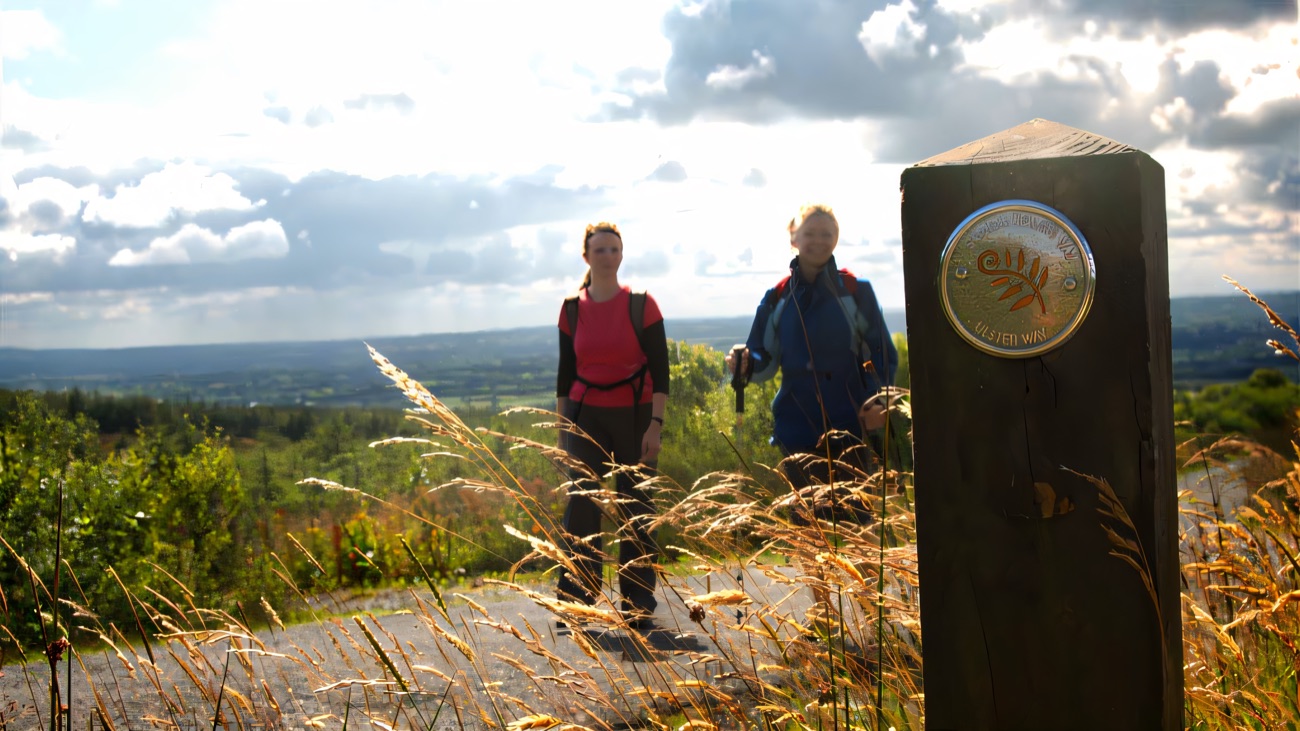 A waymarker post on the Way with the lowlands spread out below