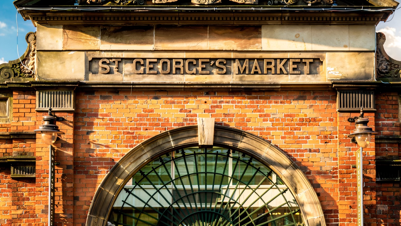 The red-brick Victorian entrance of St George's Market with its ornate stone pediment, coat of arms and arched glass gateway