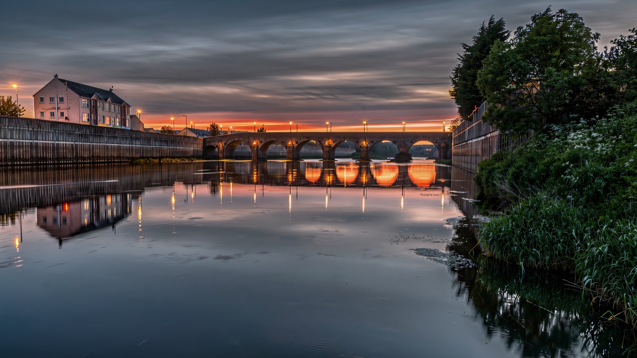 The old stone bridge reflected in the river at sunset