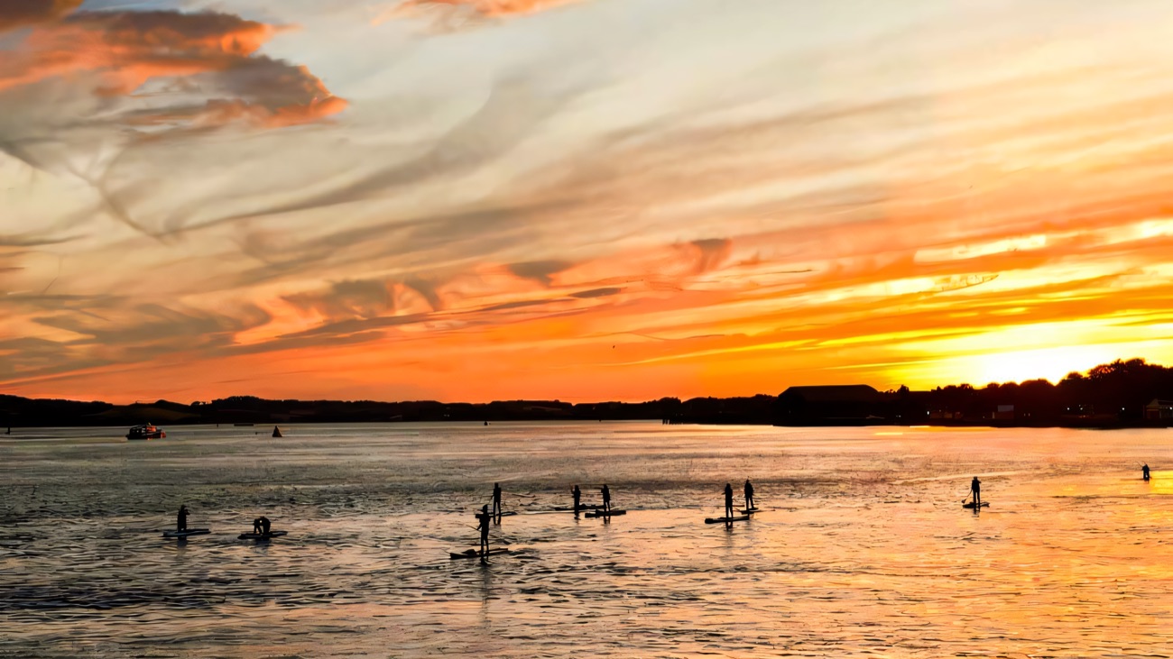 Silhouettes on the water as the sky blazes over the bay