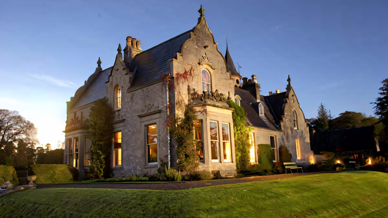Tempo Manor's grey stone Victorian-Jacobean front lit by low golden sun under a clear sky