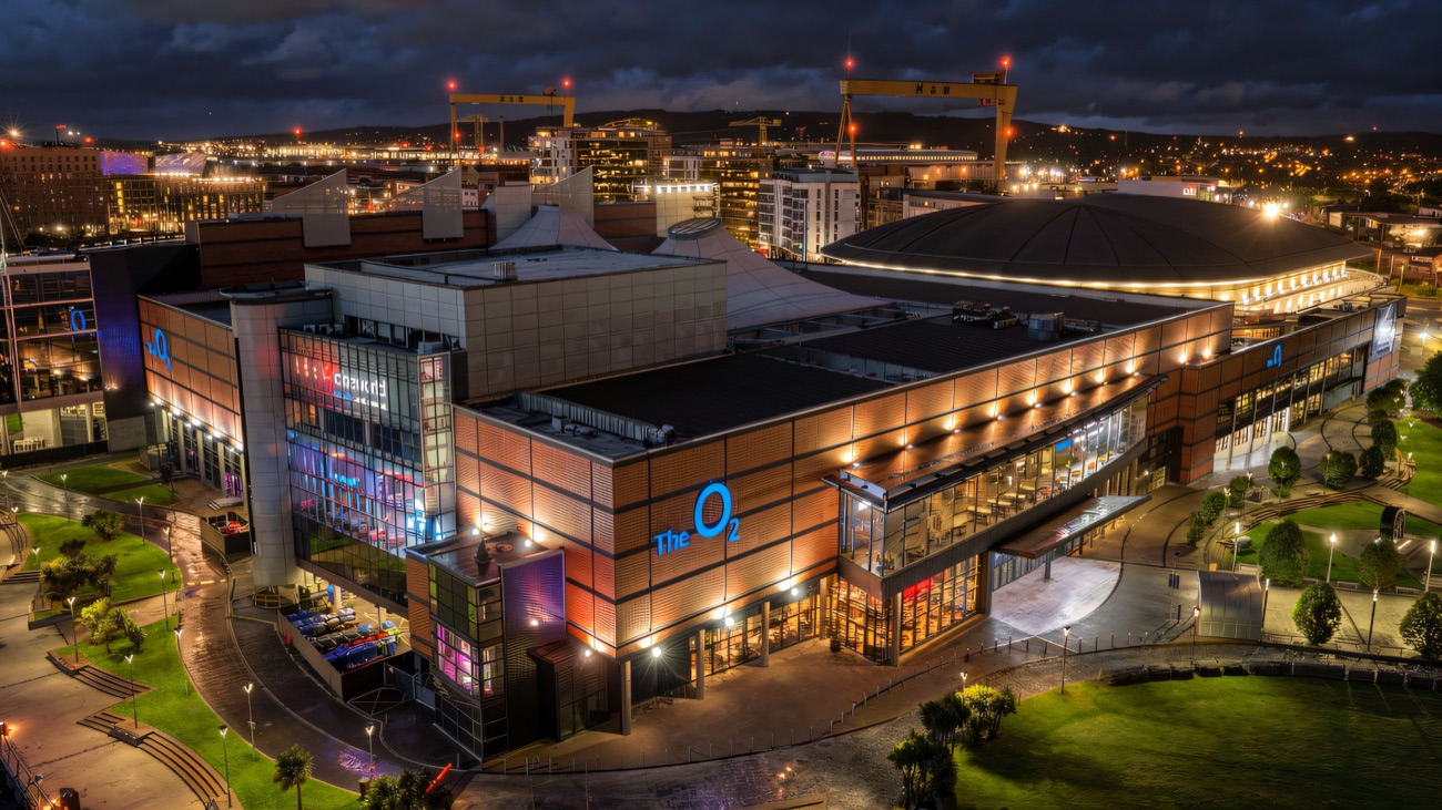 The Odyssey complex glowing at night on Belfast's Queen's Quay, the Harland & Wolff cranes behind