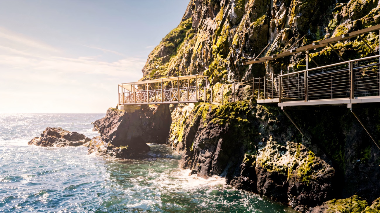 A viewing platform on The Gobbins jutting over turquoise water in bright sun