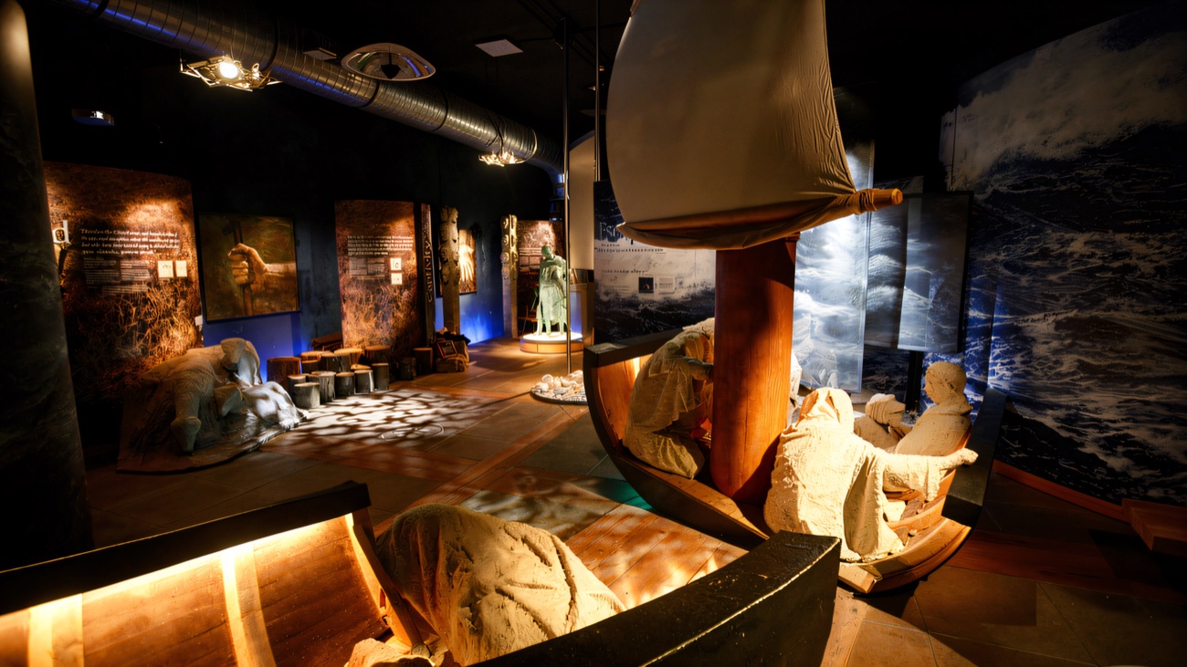 Inside the exhibition, sculpted figures voyage by boat against a storm-sea backdrop.