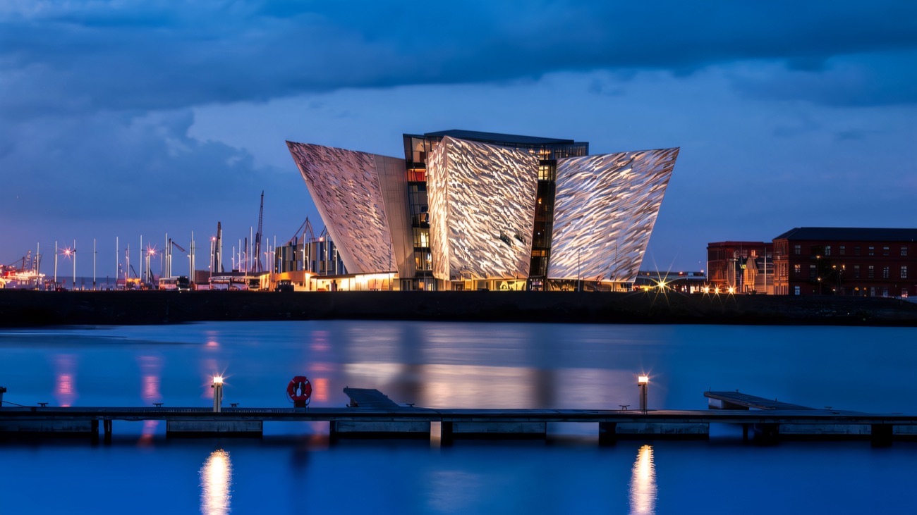 The silver hull-shaped building of Titanic Belfast glowing at night across the water