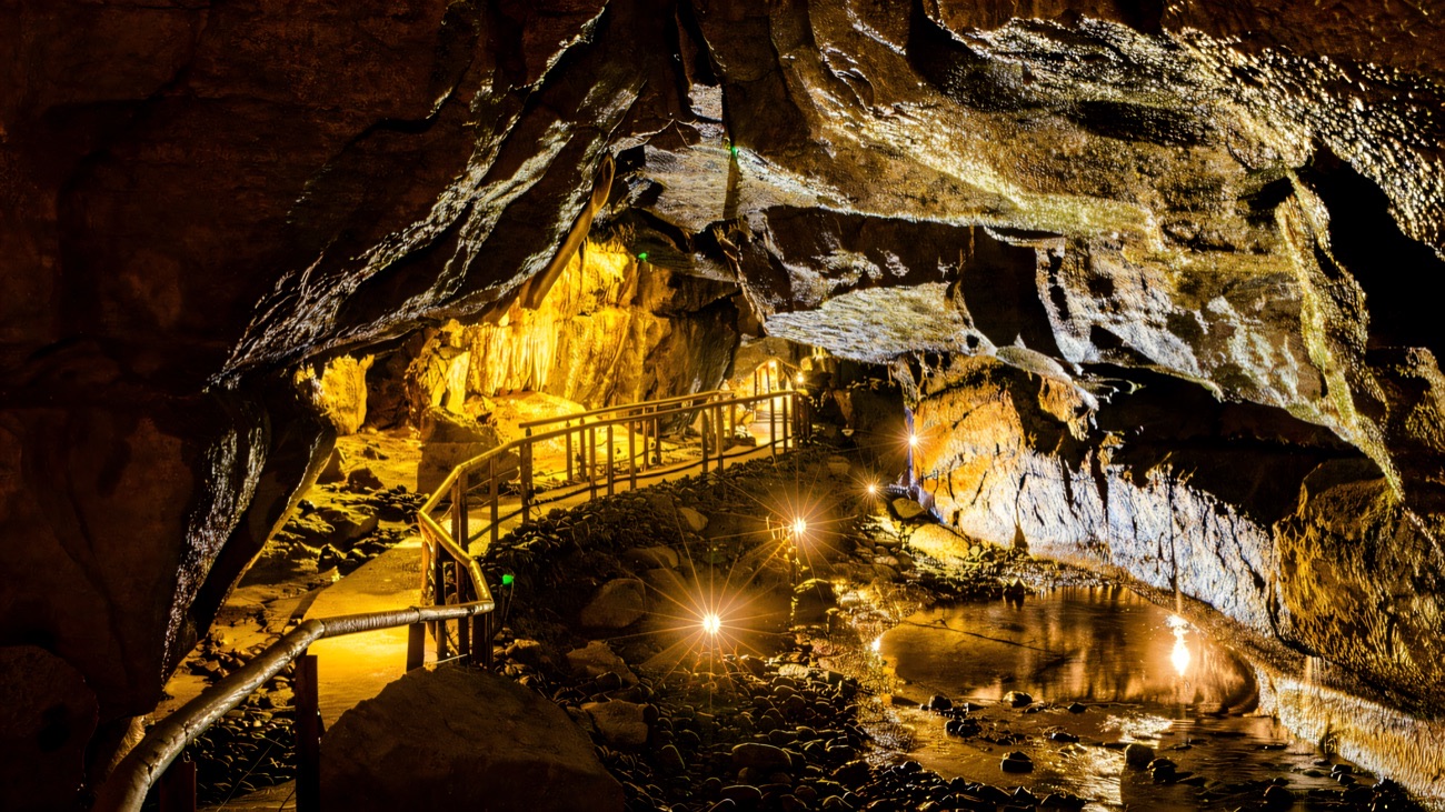 A lit walkway winding past underground pools and rock formations inside Marble Arch Caves