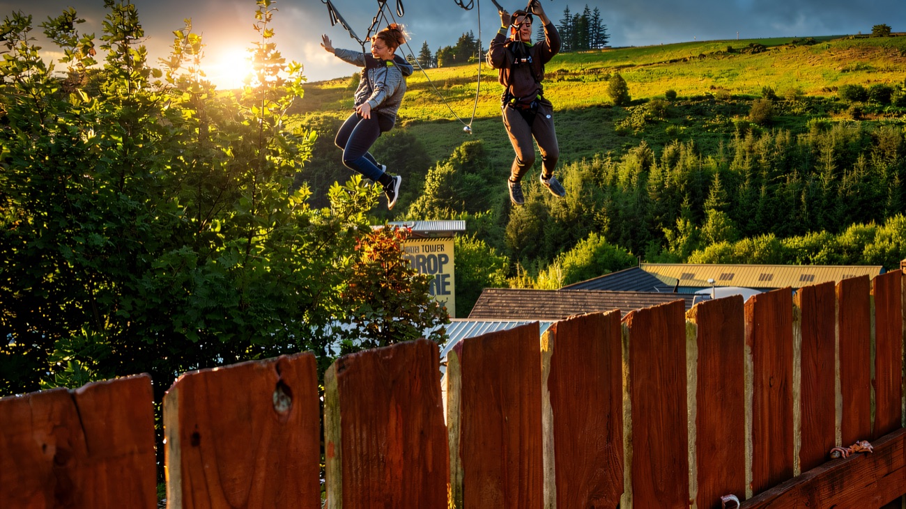 Two riders swinging out mid-air on the giant swing above the trees