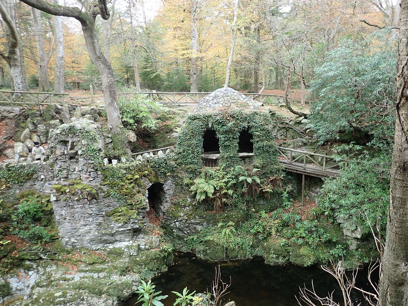 The Hermitage — an ivy-covered stone grotto beside a still pool and a wooden bridge in the woods