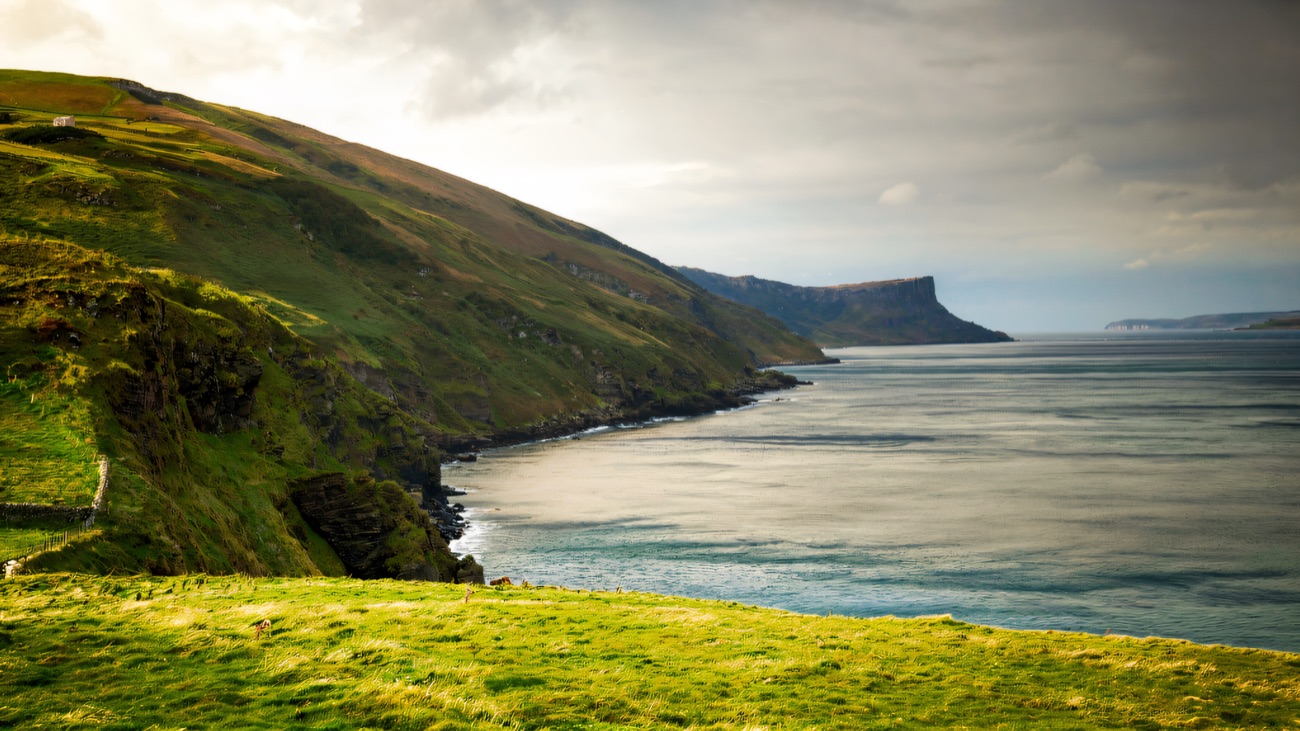 The grassy clifftop and the sweep of Murlough Bay under soft cloud