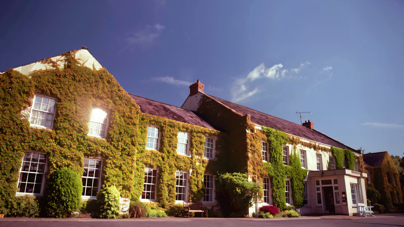 The ivy-covered stone front of Tullylagan Country House against a deep blue sky, with the main entrance below