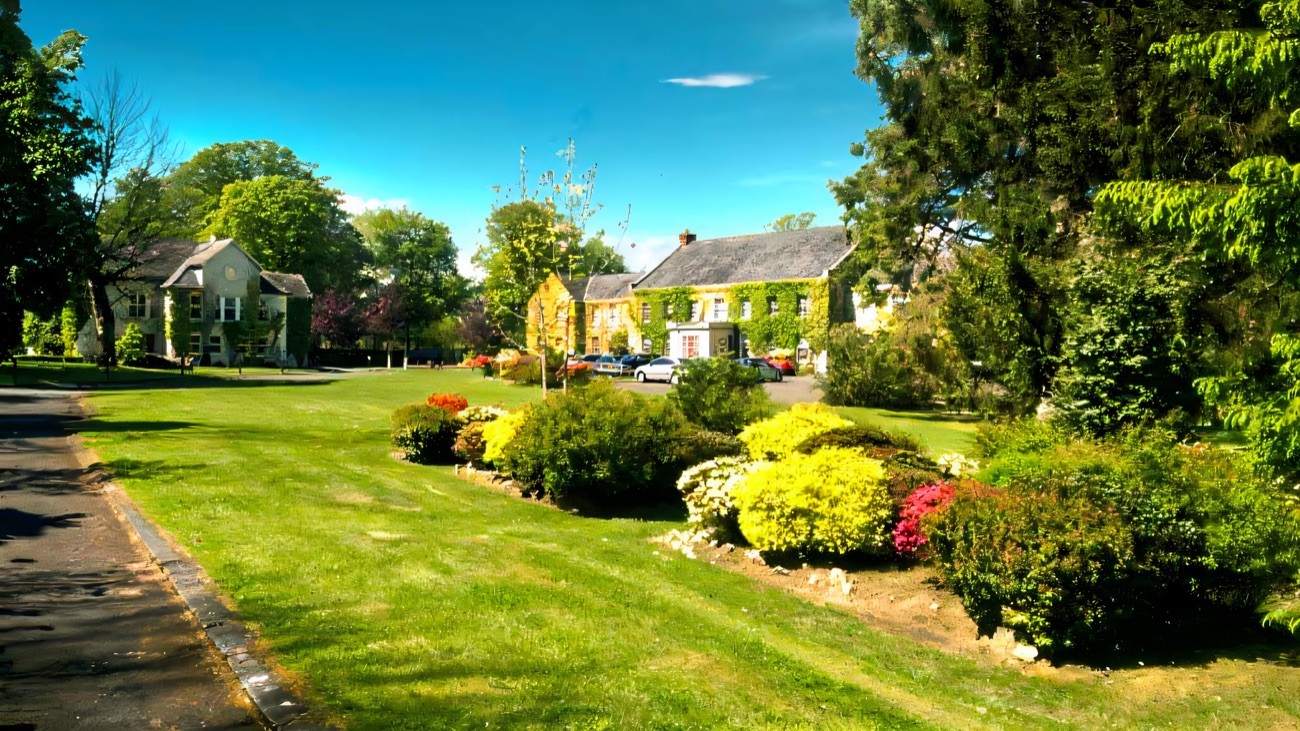 Flowering shrub borders and a manicured green lawn in the gardens at Tullylagan, with the house behind