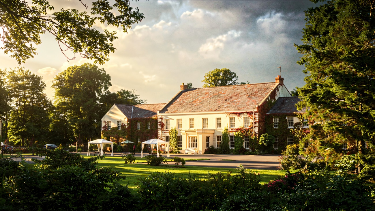 Tullylagan Country House seen across a wide lawn framed by mature trees, with parasols set out on the grass