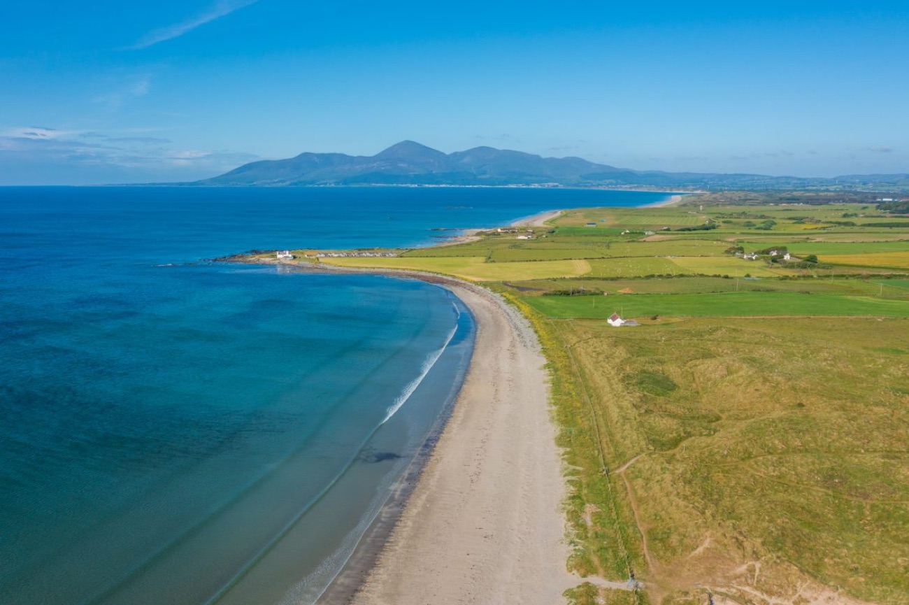 Aerial view of Tyrella Beach curving along the green coastline of Dundrum Bay with the Mourne Mountains beyond