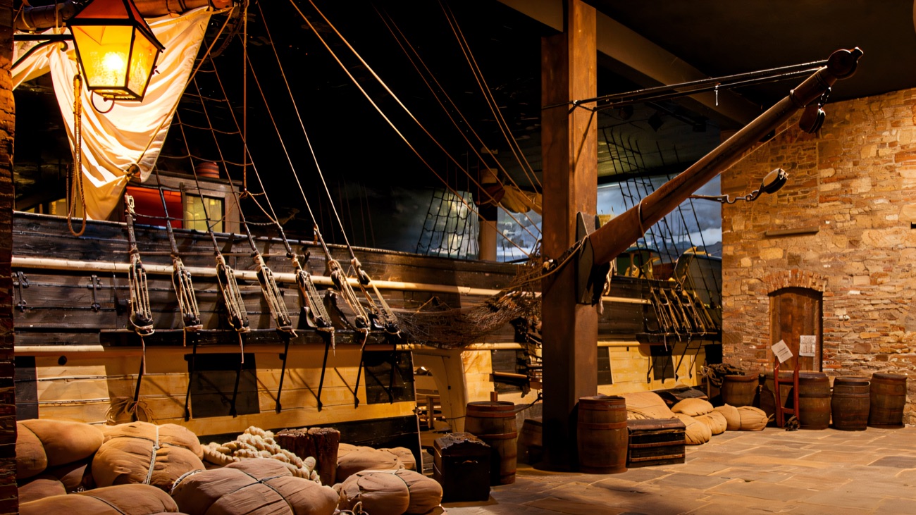 The full-size emigrant sailing ship exhibit indoors, with rigging, barrels and sacks around it